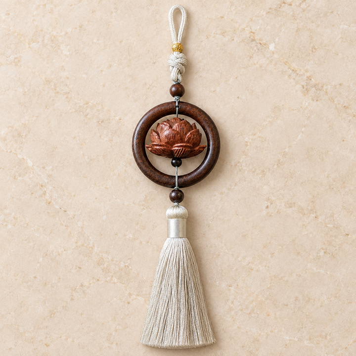 Lotus car charm with circular brown-toned frame, accent beads and gray tassel on a light background